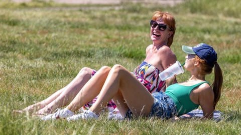 Entspannen im Sommer in der Sonne bei tollem Wetter: Zwei Frauen liegen auf einer Wiese