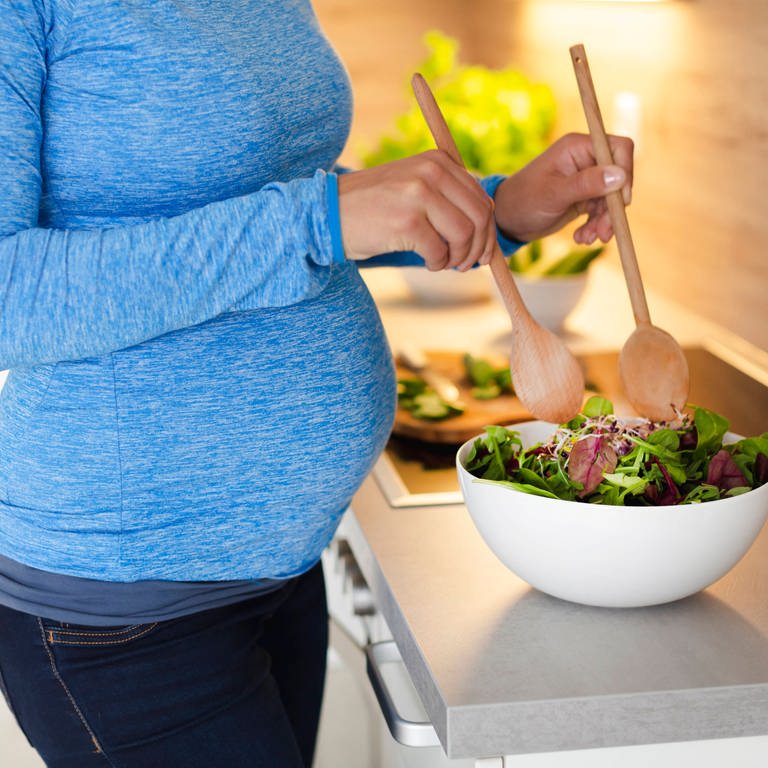 Eine Schwangere bereitet in der Küche einen Salat zu